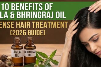 A bottle of golden Bhringraj and Amla hair oil sitting on a wooden table next to fresh green Amla fruit and raw botanical leaves.