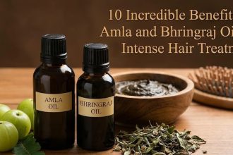 A bottle of natural Amla and Bhringraj hair oil sitting next to fresh Indian Gooseberries and green herbs on a wooden table.