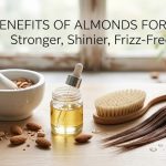 A wooden bowl filled with fresh almonds next to a bottle of almond hair oil, symbolizing natural hair care.