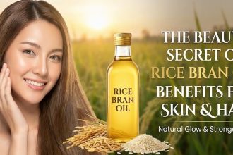 A wooden spoon filled with golden rice bran oil sitting next to a bowl of rice grains and a bottle of hair oil.